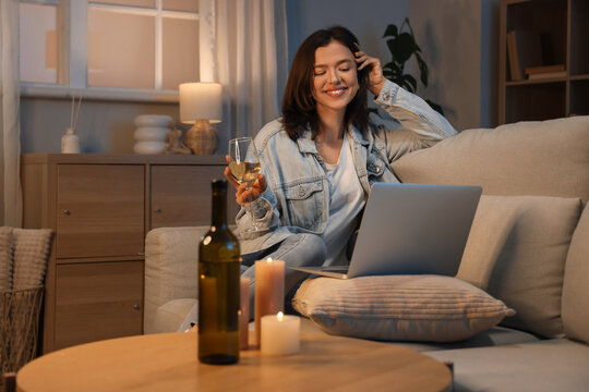 Young woman with wine having online date on sofa at home in evening - Powered by Adobe
