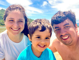 Father, mother and son in a crystal clear lagoon in front of the beach with an Atlantic forest mountain in the background during vacation. Happiness and family fun.