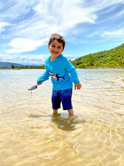 Happy boy playing in a crystal clear lagoon next to the sea with mountains and tropical vegetation of the Atlantic forest in the background in harmony with green and blue. Summer and joy