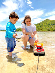 Mother playing with her son in a crystal clear lagoon in front of the beach with an Atlantic forest mountain in the background during vacation. Happiness and family fun.