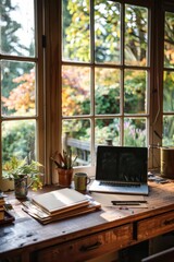 Fototapeta premium A rustic wooden desk sits by a sunlit window, showcasing a laptop, notebooks, art supplies, and a peaceful garden view; perfect for creative work or writing.