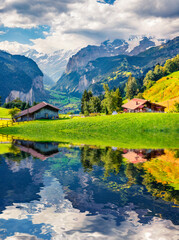 Obraz premium Green pasture and wooden chalets of Wengen village reflected in the calm waters of small mountain pond. Splendid summer scene in Swiss Alps. Beautiful morning scene of Switzerland, Europe.