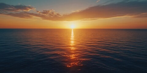 Obraz premium The sun is setting over the ocean, casting a warm glow on the water. The sky is filled with clouds, creating a serene and peaceful atmosphere