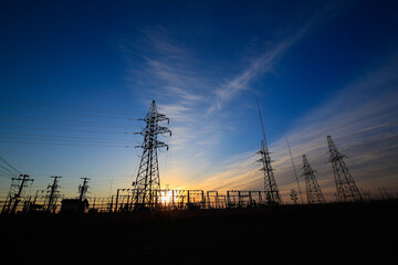Many high-voltage power towers, silhouetted against the setting sun