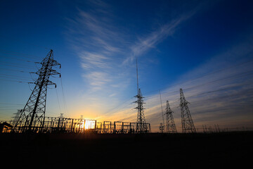 Many high-voltage power towers, silhouetted against the setting sun