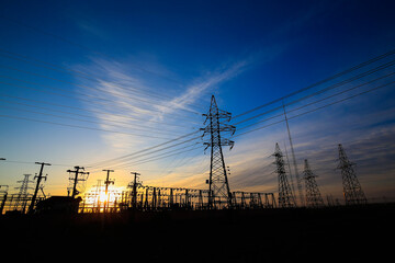 Many high-voltage power towers, silhouetted against the setting sun