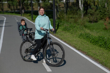 Fototapeta premium Caucasian woman riding a bicycle with her toddler son sitting behind her in a child seat. 