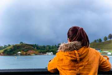 Fototapeta premium young woman on her back looking at lake in guatape, beautiful picturesque town near medellin, colombia