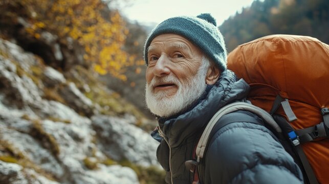 An older man wearing a blue hat and a black jacket is smiling and looking at the camera. He is carrying a backpack and he is enjoying his time outdoors
