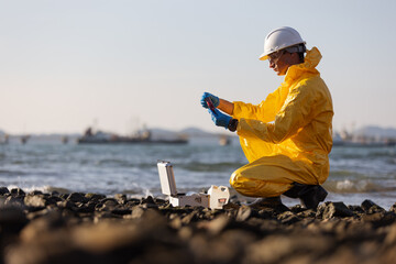 A person wearing a yellow hazmat suit and white helmet kneeling on a rocky shore,performing water...