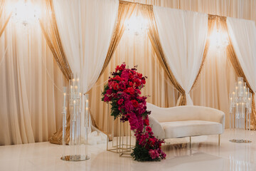 Elegant Wedding Lounge with Luxurious Floral Arrangements, Draped Gold Curtains, and Crystal Candle...