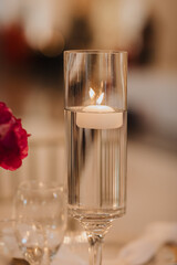 Minimalist floating candle in clear glass cylinder with warm ambient light, elegant table centerpiece detail at evening event