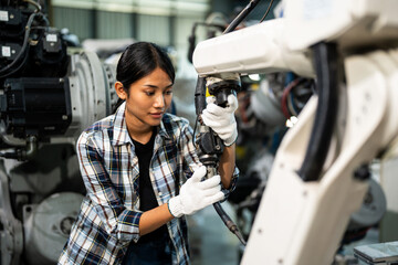 Young female engineer in a plaid shirt and gloves performing maintenance on an industrial robotic arm inside a modern manufacturing factory.