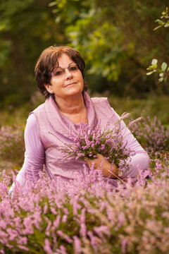 A portrait of a beautiful older woman holding a bunch of flowers outside in  the Swedish nature