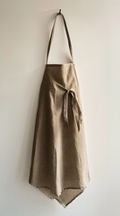 Brown linen apron hangs on a white wall with top tie.