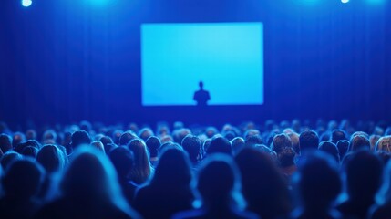 Large Crowd of People at an Event Featuring One Person on Stage in a Dimly Lit Environment with a Projector Screen in the Background