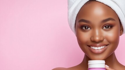 Radiant smiling woman with towel turban holding skincare product against pink background