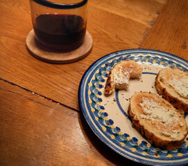 snack consisting of toasted supermarket garlic bread with soft spreadable French cheese and family style red wine in a juice glass. Not pictured: paper towel used as napkin.
