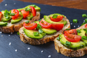 Avocado toast topped with tomato and green onion on a slice of carrot bread