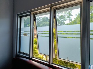 Modern glass windows with frosted privacy patterns, offering a serene view of lush green trees and...