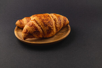 Fresh golden croissants on a wooden plate on a black background