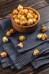 Snack, movie concept, caramelized popcorn in a wooden bowl on a wooden table