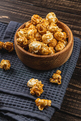 Snack concept, caramelized popcorn in a wooden bowl on a gray, wooden background