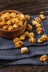 Snack concept, caramelized popcorn in a wooden bowl on a gray, wooden background