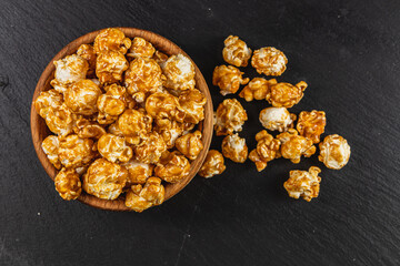 Snack concept, sweet caramelized popcorn in a wooden bowl on a black background