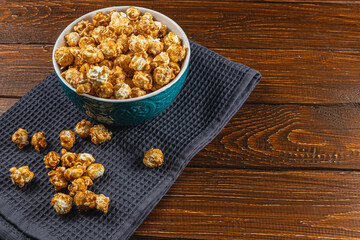 Snack concept, caramelized popcorn in a ceramic bowl on a wooden background