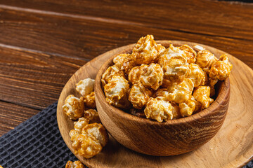 Caramelized popcorn in a wooden bowl with a plate on a wooden background