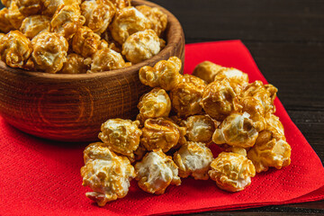 Snack, movie concept, caramelized popcorn in a wooden bowl on a red napkin