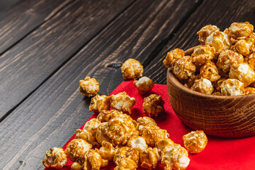 Snack, movie concept, caramelized popcorn in a wooden bowl on a red napkin