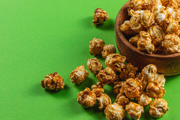 Snack concept Sweet caramelized popcorn in a wooden bowl on a green background