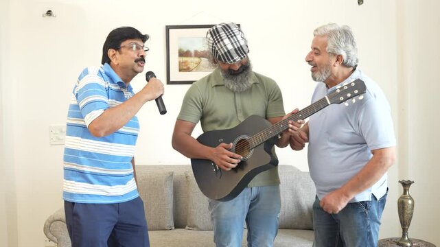 Group of senior indian friend playing guitar, singing and enjoy dancing in living room at home. Mature elderly men having party celebrate weekend reunion gathered together in house, Retirement life.