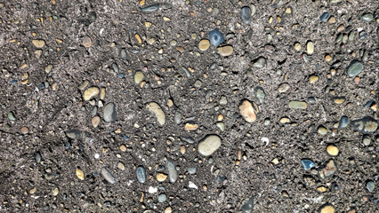 A rough concrete surface embedded with small pebbles and stones creates a textured and granular background suitable for various design applications