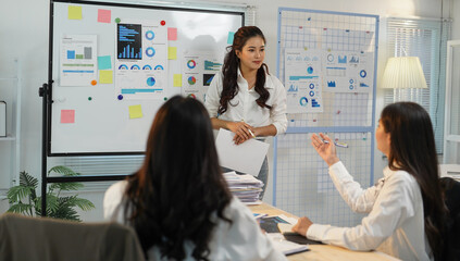 Businesswomen engaging in a discussion about business performance while analyzing financial charts displayed on a whiteboard during a collaborative meeting in the office