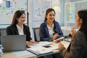 Three asian businesswomen are discussing a new project, using a calculator and a laptop in a modern office, collaborating effectively and sharing ideas for business growth and success