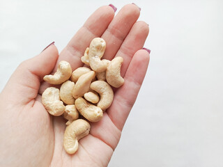 Cashew nuts in the palm of a woman's hand on a white background. Snacking on the Keto diet. A...