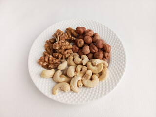 Walnuts, cashews, hazelnuts in a white plate on the table. The benefits of nuts.  The daily dose of nuts per day. The protein and fat content of nuts. Keto diet.