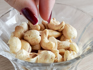 A woman's hand takes a cashew nut from a cup. A plate of cashews is on the table. A healthy snack....