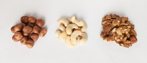 Three types of nuts on a white table. Handfuls of cashews, walnuts and hazelnuts on the table. The benefits of different types of nuts.