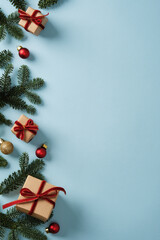 Christmas gifts made of brown kraft paper with red velvet ribbons and sprigs of evergreen fir tree on blue background. Space for your text.