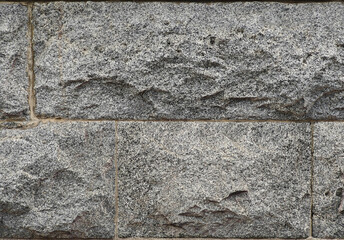 Close-up of a stone wall made from rough, gray rectangular blocks with visible textures and natural patterns, arranged horizontally.