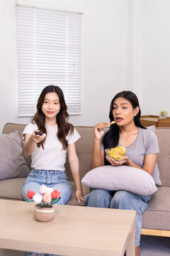 Two friends enjoying snacks while watching TV in a cozy living room.