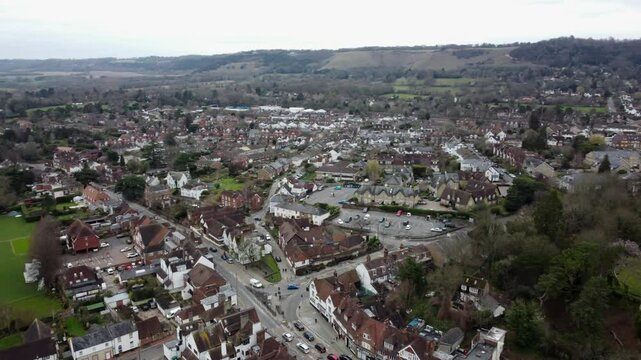 Dynamic parallax aerial footage of Reigate town and Priory Park. Showcasing houses, sports fields, and surrounding greenery under a cloudy sky. A blend of suburban charm and open countryside.