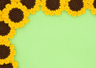 Close up top view of hand crochet yarn sunflowers on a green mat with copy space. flowers forming a corner border.