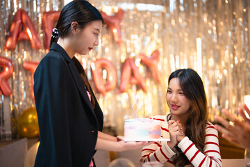 Asian people friends having celebration birthday party together at home with food and drink. Woman excited with birthday cake make a wish and blowing birthday candle with happiness.