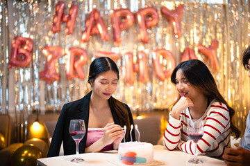 Asian people friends having celebration birthday party together at home with food and drink. Woman excited with birthday cake make a wish and blowing birthday candle with happiness.