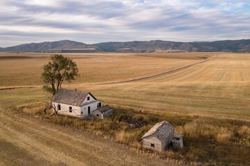 Abandoned farmhouse and outbuildings on a harvested field, nestled in a valley, overlooking the rolling hills. Empty, weathered structures, a testament to time. , Ririe, Idaho, USA.